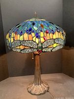 Full view of the table lamp showing stained glass shade with dragonfly design and metal base.