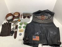 Full view of all items including leather vest, belts, belt buckles, gloves, watches, sunglasses, and smaller accessories arranged on a flat surface.