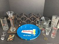 Full lot view showing bicycle chain wine rack, Ballantine beer tray, various mugs, glasses, and shot glasses displayed on dark table surface.