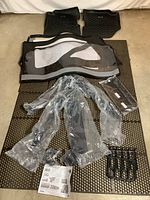 Photo showing Jeep Wrangler soft top fabric with clear plastic windows, frame parts in plastic packaging, two rubber floor mats, and installation instructions laid out on a mat.