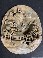 Carved soapstone Asian relief with stand, showing detailed landscape carving with architecture and natural elements in round shape.