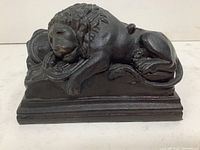 Black stone lion sculpture in reclining position on rectangular base