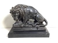 Front view of black marble lion statue showing detailed mane, muscular body, and rectangular stepped base with some surface scratches.