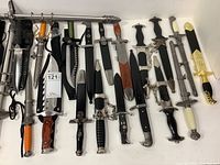 Overhead view of 13 blades arranged in white box showing variety of handles, guards and sheaths