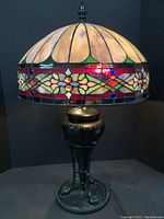 Full view of stained glass lampshade lit showing warm cream petals, red, blue, green, and amber accent pieces.