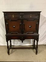 Front view of the dark wood occasional cabinet with two drawers at the top and double doors below on turned legs.