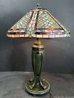 Front view of entire Tiffany-style table lamp showing stained glass shade and green base with claw feet.