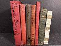 Front view of seven vintage hardcover books arranged side by side showing spine titles including Etiquette for Moderns, Gentlemen Prefer Blondes, Ethics of Marriage, Good Morals and Gentle Manners, The Romance of Exploration and Emergency First Aid from Stanley to Byrd, Physiology of Marriage, Reveries of a Bachelor.