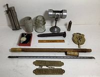 Overview of a group of vintage metal and glass curiosities including the lock, thermometer, insulator, railroad spike, metal rods, small containers, and signage.