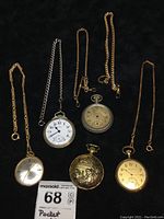 Full view of 7 pocket watches and their chains displayed on black background.