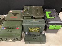 Overview of all boxes including two green first aid boxes, several green metal ammo cans with cartridge count stencils, and a black plastic Zombie Ammo Can with green handle.