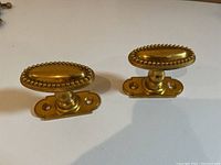 Photo showing two oval brass doorknobs with beaded edges on a white surface, front view.