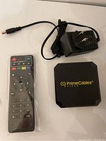 PrimeCables 4K Smart TV box, remote control sealed in plastic, and power adapter with cable resting on white surface.