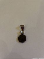 Front view of silver charm showing antique weathered coin and oval blue stone above it.