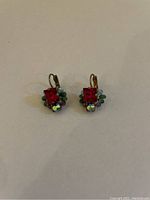Pair of antique earrings displayed on plain background showing front view with red square stones and multicolor bead cluster accents.