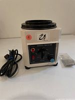 Front view of white magnetic barrel tumbler with control panel, power cord, and bag of metal pins.