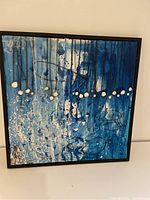 Front view of square contemporary abstract painting with blue, white, and black paint on canvas in a simple frame.