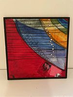 Front view of framed abstract painting with red, blue, yellow and green colors and black and white accents.