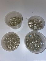 Four clear containers filled with various clear crystal drops of different sizes and shapes under bright light on a white surface.