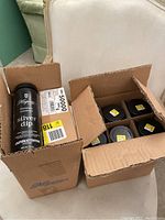 Open cardboard boxes showing twelve black cylindrical containers of Hagerty Silver Dip flatware cleaning solution. Each container is sealed and stored upright with dividers in the box.