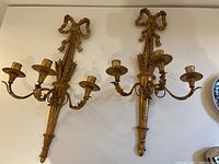 Two gold-painted wood wall sconces side by side, showing bow top and three-arm design
