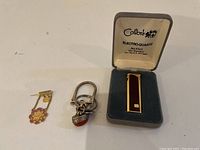 Photo showing the lapel pin, silver keychain with charm, and Colibri Electroquartz lighter in box