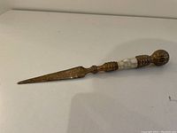 Side view of the letter opener knife showing the rusted blade and the white segmented inlay handle with a rounded metal end.