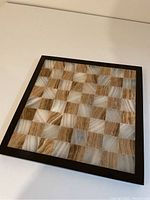 Top angled view of marble chess board showing alternating white and brown marble squares framed in black.
