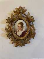 Front view of ornate gilded wood frame with oval miniature portrait of a woman.