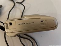 Bottom view of silver Olympus camera showing 'OLYMPUS TOKYO JAPAN' engraving and serial number '2574912'.