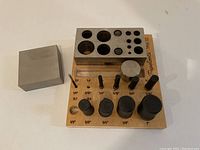 Jewelry gold press showing wooden base with metal block, pins, and holes with size labels