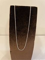 Silver chain necklace displayed vertically on a black velvet stand, showing the necklace's shine and general form.