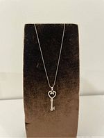 Key pendant necklace displayed on black velvet stand showcasing the full length and design.