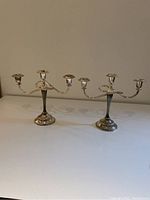 Two silver plated three-arm candelabras showing general form and condition with tarnishing and wear.