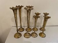 Front view of all eight brass candle holders arranged by height on a white surface, showing the fluted tops and round bases.