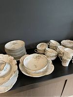 Stack of dinner plates, salad plates, teacups, and cream soup bowls showing floral pattern with gold trim.