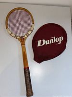 Top view of the Dunlop Maxply wooden tennis racket and its burgundy cover with Dunlop logo.