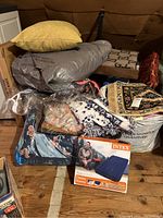 Cluster of pillows, blankets, and boxed Twin Intex Classic Downy air mattress on attic floor with wood flooring and attic walls visible