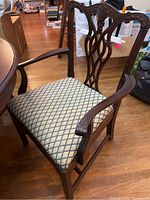 Full view of an armchair with carved wooden back and upholstered seat in diamond pattern fabric.