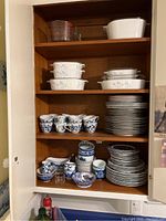 Shelves filled with Shadow Iris Corning Ware casserole dishes with lids stacked on top shelves. Blue Danube cups, saucers and plates stacked below. Additional decorative bowls and small glass cups on bottom shelf.