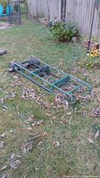 Full view of green metal appliance dolly lying on grass with visible frame and wheels