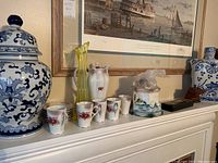 Wide shot showing all items on mantle including ginger jars, cups, decanter, vase, small box, and books.