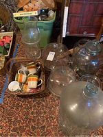 Photo showing large glass jars, a beverage dispenser, and wicker basket with mugs