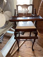 Full view of the wooden high chair showing wooden tray, carved backrest, light cushioned seat and armrests in attic setting