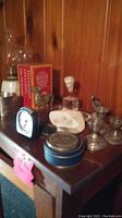 View of shelf with silver candle holders, clock, blue tin box, wooden bird figurine, shell decoration, small glass lantern, and red books.
