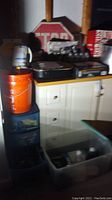 Photo showing Master Cook portable grill and single burner butane stove placed on a white cabinet, with a large orange resin bin nearby.