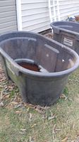 Gray Rubbermaid water/feed tub outdoors showing overall shape and size, with some dirt and leaves around.