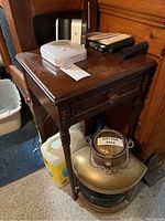 Wooden side table with carved drawer front and tapered legs. Surface has scratches. Items on top and underneath not included.