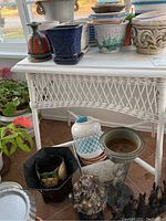 Full view of the white wicker table with various flower pots and decorative items placed on and below the table, showing structure and stained wood top.