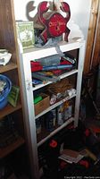 White wooden shelf unit with various tools including pliers, clamps, cable ties, a crab-shaped birdhouse in red paint, and assorted tools and materials.